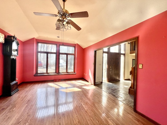 unfurnished living room with lofted ceiling, hardwood / wood-style floors, and baseboards