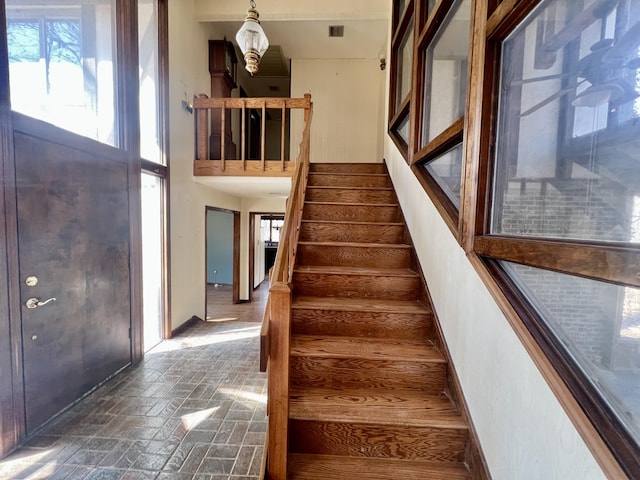 foyer entrance with brick floor, a high ceiling, stairway, and baseboards