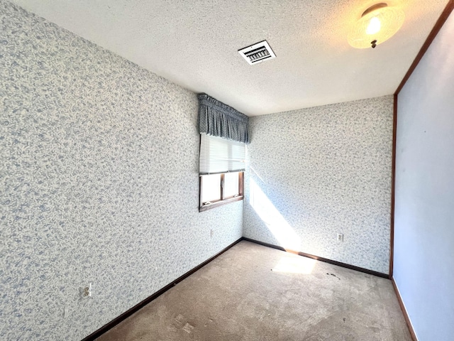 carpeted spare room featuring a textured ceiling, wallpapered walls, visible vents, and baseboards