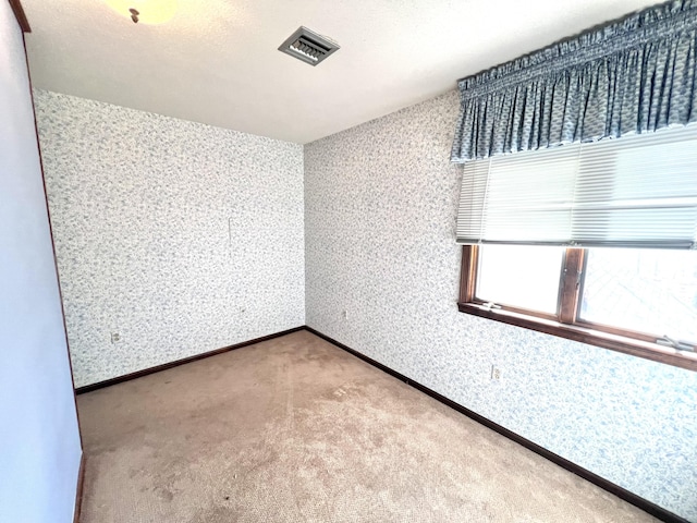 empty room featuring wallpapered walls, baseboards, visible vents, and carpet flooring