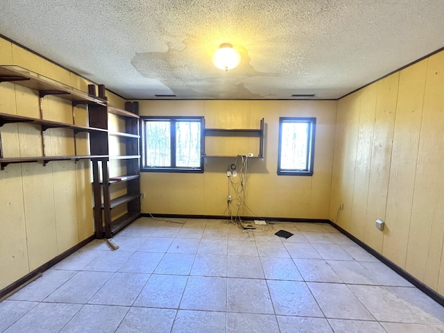 empty room featuring light tile patterned floors, baseboards, a textured ceiling, and wood walls