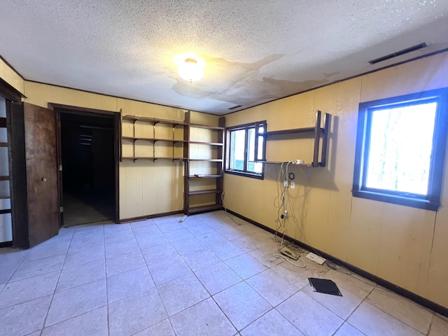 empty room featuring a textured ceiling, light tile patterned floors, visible vents, and baseboards