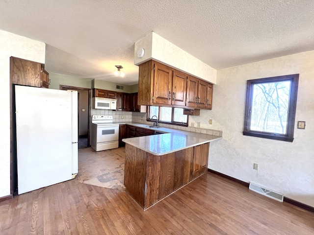 kitchen featuring visible vents, a sink, wood finished floors, white appliances, and a peninsula