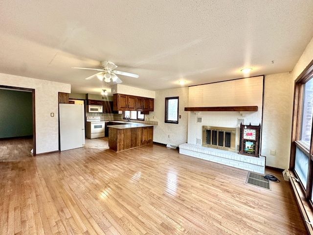 unfurnished living room featuring ceiling fan, a brick fireplace, light wood-style floors, and a textured ceiling