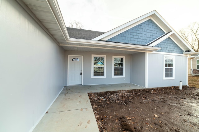 view of exterior entry with covered porch and a shingled roof