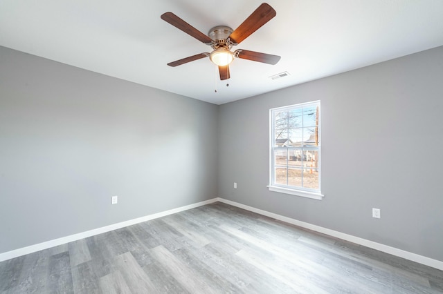 spare room with a ceiling fan, visible vents, baseboards, and wood finished floors