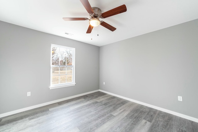 empty room featuring a ceiling fan, visible vents, baseboards, and wood finished floors