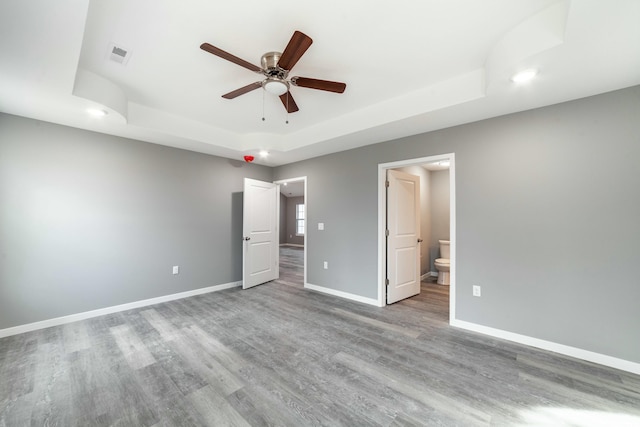 unfurnished bedroom with connected bathroom, wood finished floors, visible vents, baseboards, and a raised ceiling