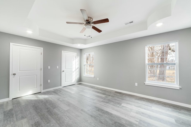 unfurnished bedroom with baseboards, visible vents, a raised ceiling, and wood finished floors