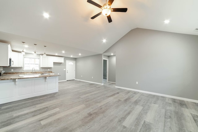 kitchen featuring a peninsula, a sink, baseboards, white cabinets, and light wood-type flooring