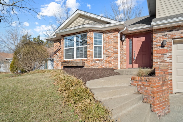 property entrance with a shingled roof, brick siding, a yard, and an attached garage