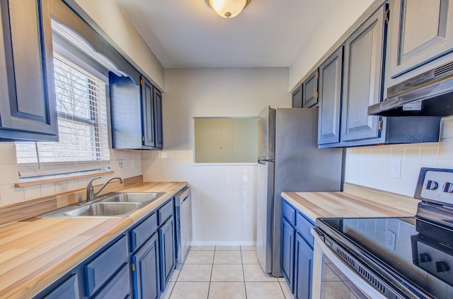 kitchen with light tile patterned floors, under cabinet range hood, a sink, wooden counters, and appliances with stainless steel finishes