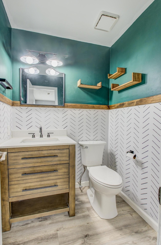 half bathroom featuring visible vents, vanity, toilet, and wood finished floors