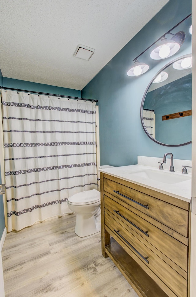 full bath with a textured ceiling, vanity, wood finished floors, and toilet