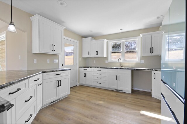 kitchen with light wood-style flooring, a sink, white cabinetry, dark stone countertops, and decorative light fixtures