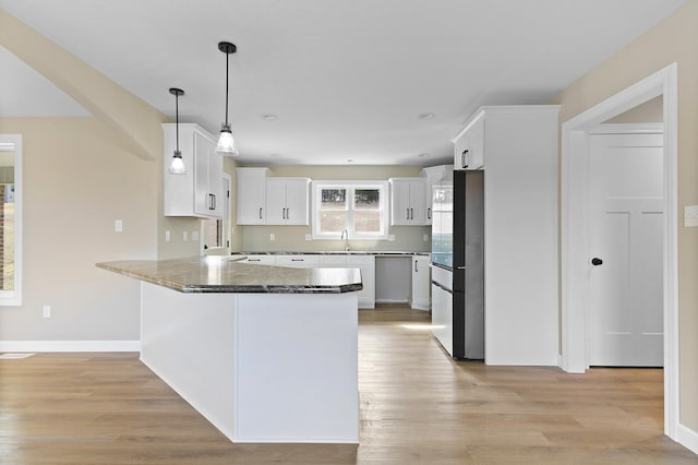 kitchen featuring a peninsula, a sink, white cabinetry, freestanding refrigerator, and light wood finished floors