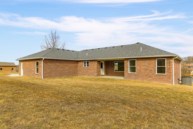 back of house with a shingled roof, a lawn, cooling unit, and brick siding