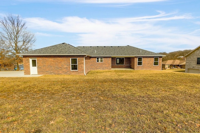 rear view of property with roof with shingles, a lawn, and brick siding