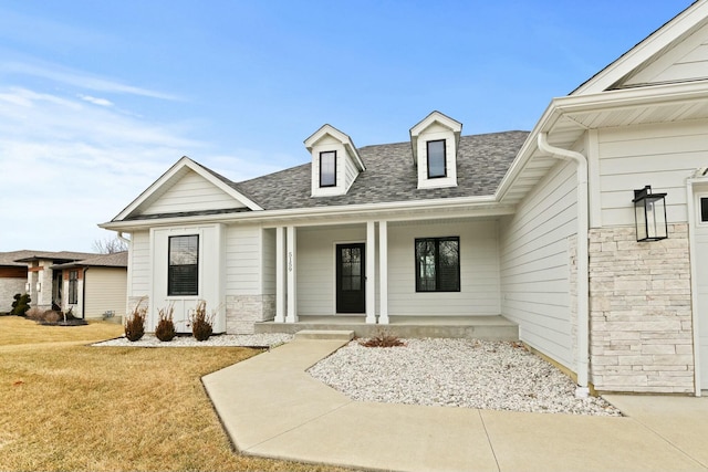 view of front of property with covered porch, stone siding, roof with shingles, and a front yard