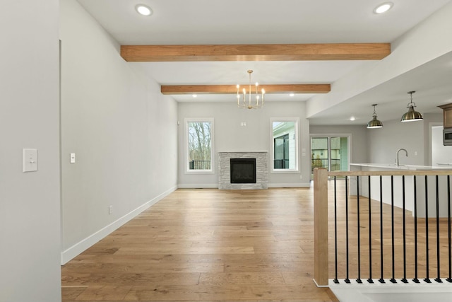 unfurnished living room featuring beam ceiling, a sink, light wood-style flooring, and baseboards