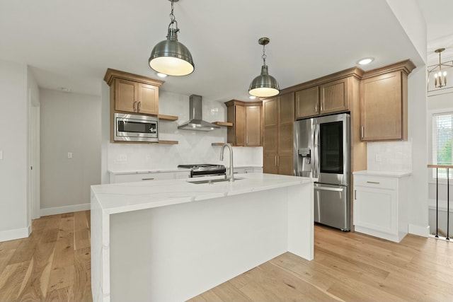 kitchen featuring light wood finished floors, decorative backsplash, wall chimney exhaust hood, appliances with stainless steel finishes, and a sink