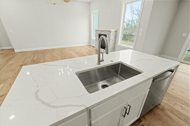 kitchen featuring light wood-style floors, light stone counters, a sink, and dishwasher