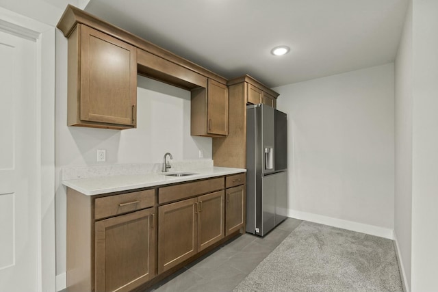 kitchen with light countertops, light tile patterned flooring, a sink, stainless steel fridge, and baseboards