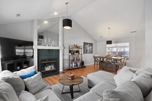 living area featuring wood finished floors, visible vents, baseboards, vaulted ceiling, and a tiled fireplace