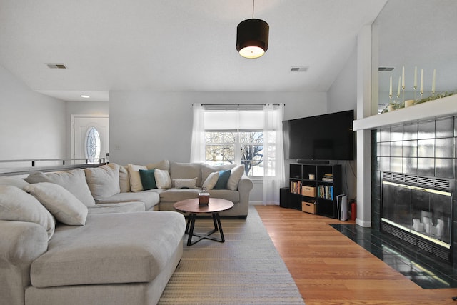 living area featuring a fireplace with flush hearth, visible vents, and wood finished floors