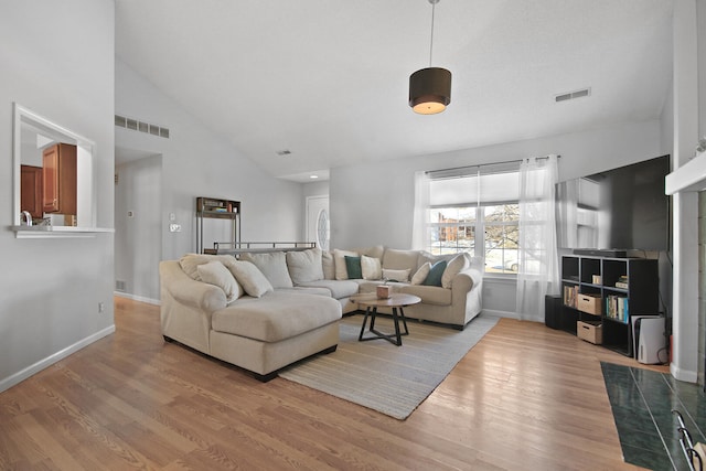 living area with light wood finished floors, baseboards, visible vents, and high vaulted ceiling