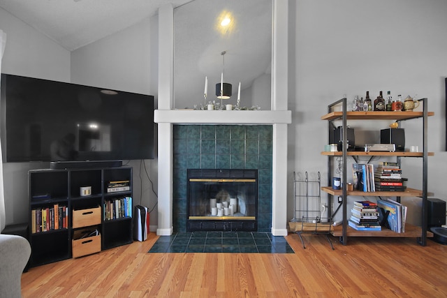 living room with lofted ceiling, a tiled fireplace, and wood finished floors