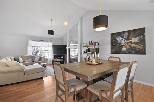 dining area featuring high vaulted ceiling, light wood-style flooring, and baseboards