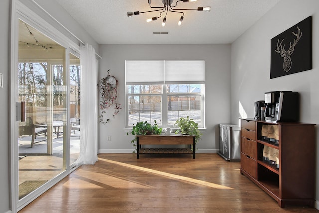 living area with visible vents, a textured ceiling, baseboards, and wood finished floors