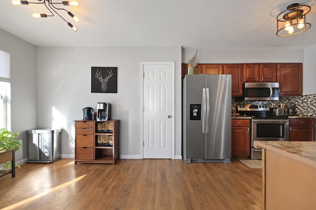 kitchen with baseboards, decorative backsplash, appliances with stainless steel finishes, wood finished floors, and a textured ceiling