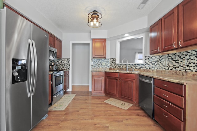 kitchen featuring a textured ceiling, light wood-style flooring, a sink, appliances with stainless steel finishes, and tasteful backsplash