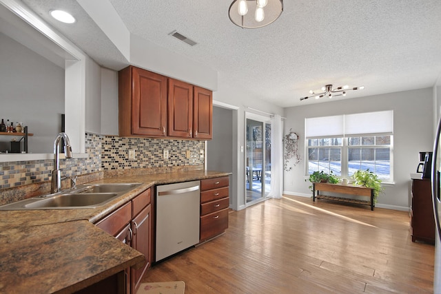 kitchen featuring tasteful backsplash, visible vents, wood finished floors, stainless steel dishwasher, and a sink