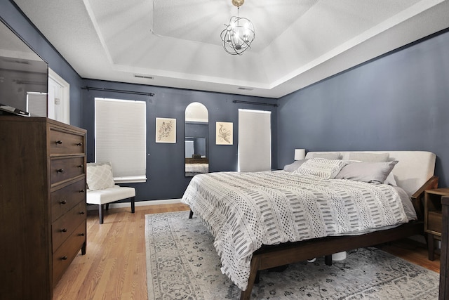 bedroom with arched walkways, a chandelier, visible vents, light wood finished floors, and a tray ceiling