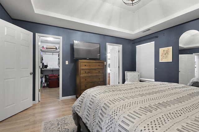 bedroom featuring arched walkways, a walk in closet, a closet, visible vents, and light wood-style floors