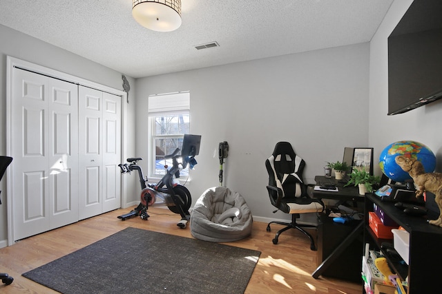 workout room featuring a textured ceiling, wood finished floors, visible vents, and baseboards