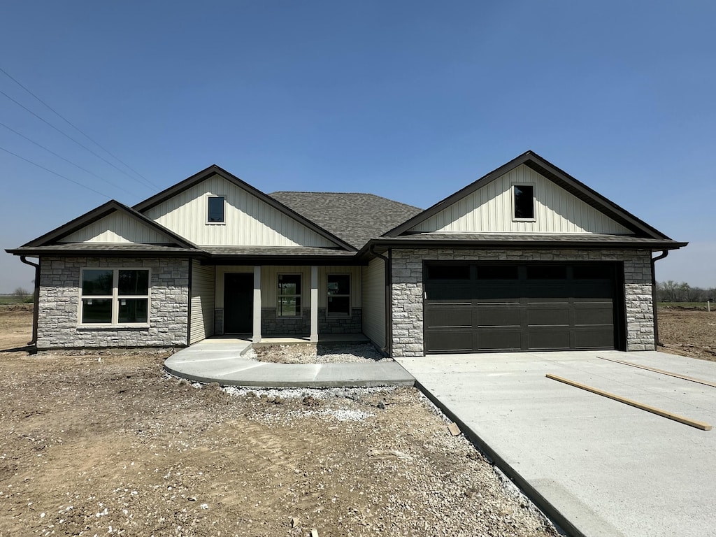 view of front facade featuring concrete driveway, roof with shingles, stone siding, an attached garage, and covered porch