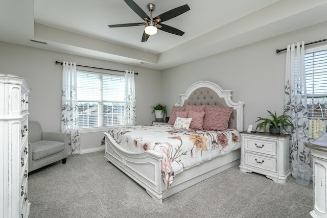 bedroom with ceiling fan, light colored carpet, visible vents, baseboards, and a raised ceiling