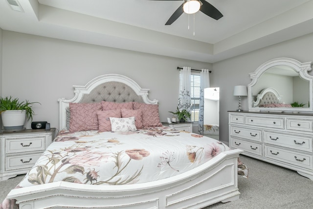 bedroom with ceiling fan, a tray ceiling, visible vents, and light colored carpet