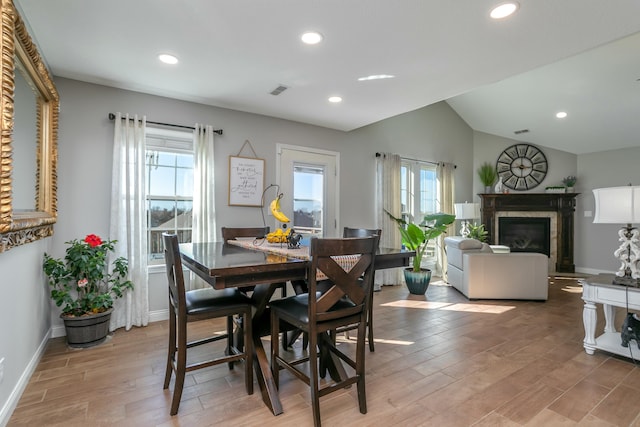 dining area featuring lofted ceiling, a glass covered fireplace, a wealth of natural light, and light wood-style floors