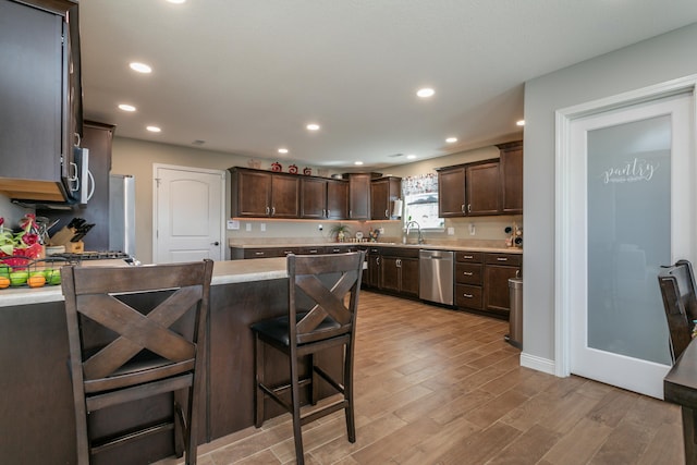 kitchen featuring appliances with stainless steel finishes, dark brown cabinetry, a peninsula, and light wood finished floors