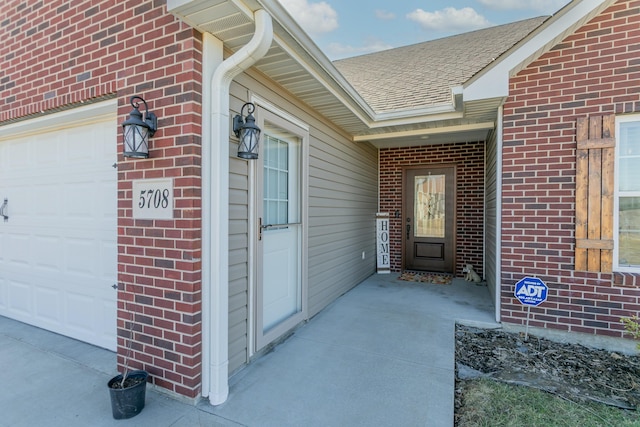 property entrance featuring a shingled roof, an attached garage, and brick siding