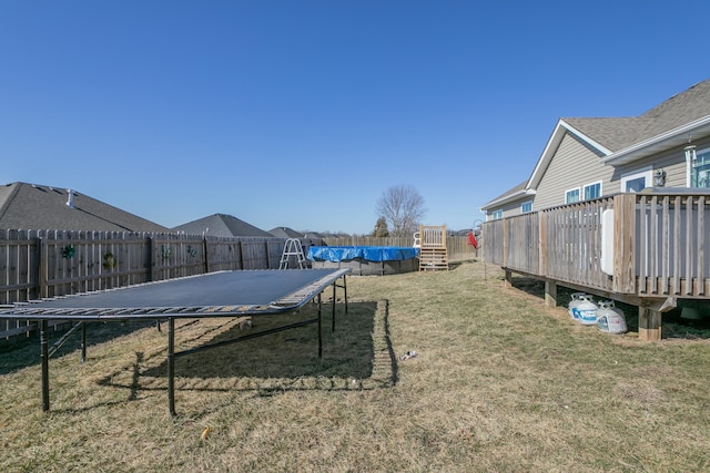 view of yard featuring a trampoline, a fenced backyard, and a deck