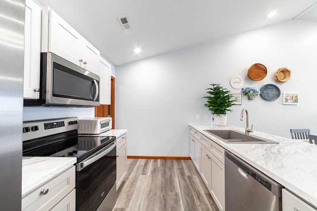 kitchen featuring light stone counters, light wood-style flooring, appliances with stainless steel finishes, white cabinets, and a sink