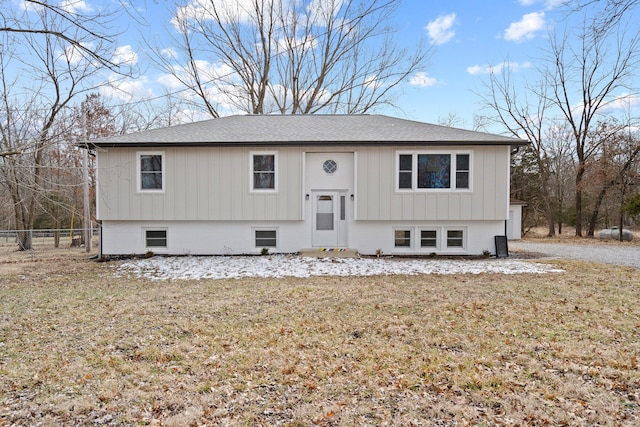 raised ranch with a shingled roof, fence, and a front yard