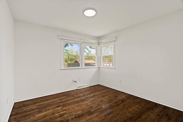 unfurnished room with baseboards, visible vents, and dark wood-type flooring