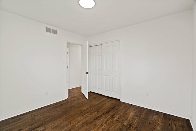 unfurnished bedroom featuring dark wood-type flooring, a closet, visible vents, and baseboards